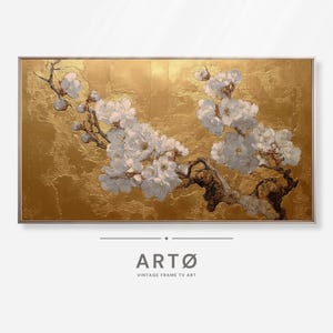 May include: A framed painting of white blossoms on a brown branch against a gold background. The artwork has a textured appearance and is set in a silver frame. The text "ARTØ VINTAGE FRAME TV ART" is at the bottom.