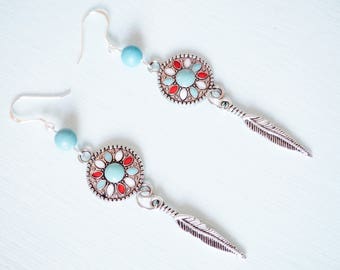 May include: A pair of silver-toned earrings with a turquoise, red, and white circular design. Each earring features a feather charm and a light blue bead. The earrings have a hook closure.