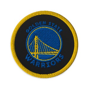 Peut inclure: Un écusson brodé circulaire représentant le logo des Golden State Warriors. Le motif comprend un pont jaune centré sur un cercle bleu, entouré d'un fond noir et d'une bordure jaune épaisse. Le texte Golden State Warriors est brodé en bleu.