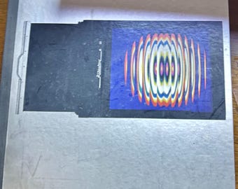 Könnte beinhalten: Ein silberfarbenes Buch mit einem farbenfrohen abstrakten Design auf dem Cover. Das Cover hat das Wort "Color" in Schwarz unten rechts gedruckt.