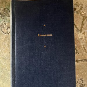 May include: A dark blue hardcover book with gold lettering that reads "Emerson" on the front cover. The book has two gold lines at the top and bottom of the cover.