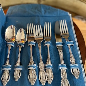 May include: A set of silver-plated cutlery in a blue velvet case. The set includes two spoons, four forks, and a knife.