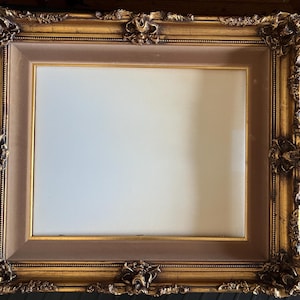 May include: Ornate gold-colored picture frame with a brown inner border. The frame has detailed floral and scrollwork designs on the corners and edges. The frame is empty, ready for a photo or artwork.