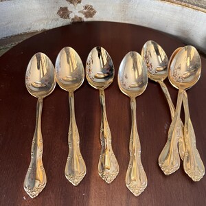 May include: Set of six gold-tone teaspoons with ornate handles. The spoons have a classic design and are perfect for everyday use.