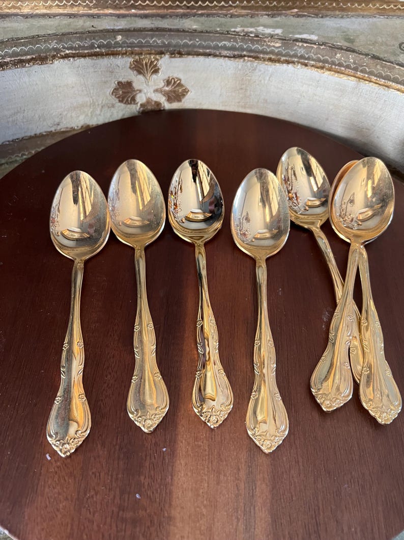May include: Set of six gold-tone teaspoons with ornate handles. The spoons have a classic design and are perfect for everyday use.