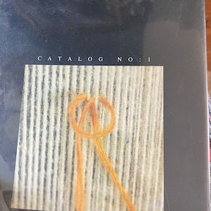 May include: A catalog cover for Turkish Handwoven Carpets. The cover features the text "TURKISH HANDWOVEN CARPETS" at the top and "CATALOG NO: 1" in the center. The image shows a close-up of weaving with orange yarn.