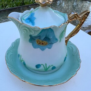 Antique porcelain creamer with saucer. Beautiful details of blue and green flowers, 22k gold rim. 5&quot; tall 5&quot; wide sauce 5&quot; diameter.