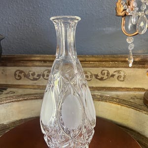 May include: A clear glass decanter with a textured, cut-glass design. The decanter features frosted oval accents and a slender, elongated shape. The decorative bottle is likely used for serving beverages.