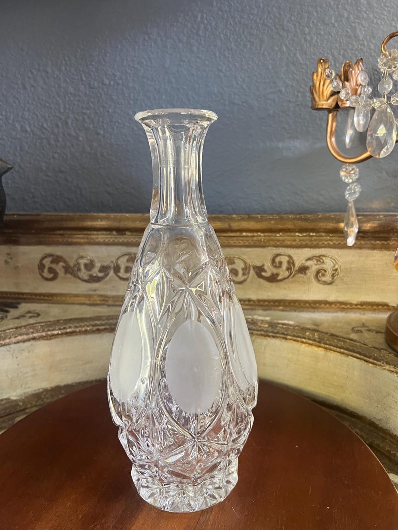 May include: A clear glass decanter with a textured, cut-glass design. The decanter features frosted oval accents and a slender, elongated shape. The decorative bottle is likely used for serving beverages.