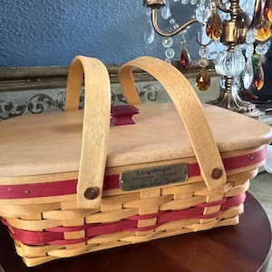 Peut inclure: Un panier Longaberger Christmas Collection édition 1993 Holiday Cheer. Le panier est en bois tressé avec un ruban rouge. Il a un couvercle en bois et deux poignées arquées. Une étiquette métallique est attachée à l'avant.