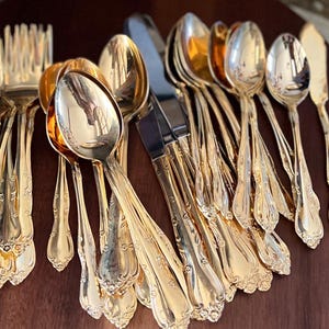 May include: A set of gold-plated silverware, including forks, spoons, and a butter knife, arranged on a wooden surface.