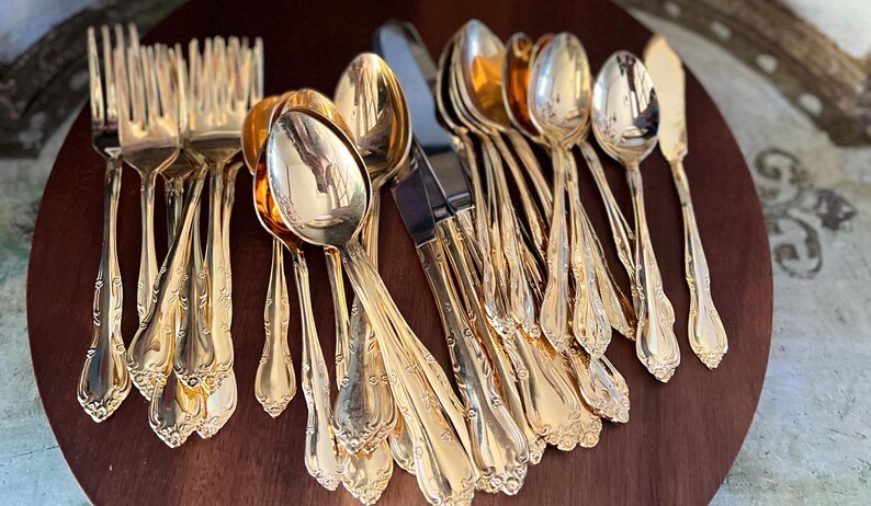 May include: A set of gold-plated silverware, including forks, spoons, and a butter knife, arranged on a wooden surface.