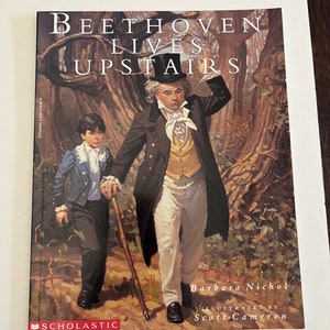 Puede incluir: Una portada de libro Scholastic con una ilustración de un hombre y un niño caminando por un bosque. El hombre lleva un abrigo negro, pantalones blancos y un chaleco amarillo. Lleva un sombrero de copa en la mano. El niño lleva una chaqueta azul y pantalones negros. El título del libro es "Beethoven Lives Upstairs".