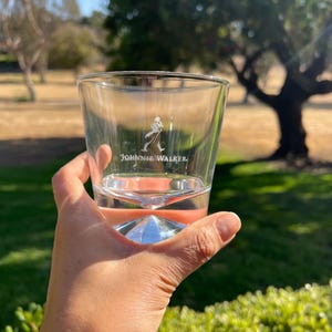 Pu&ograve; includere: Un bicchiere di vetro trasparente con una base a forma di diamante. Il bicchiere ha il logo Johnnie Walker inciso sul lato.