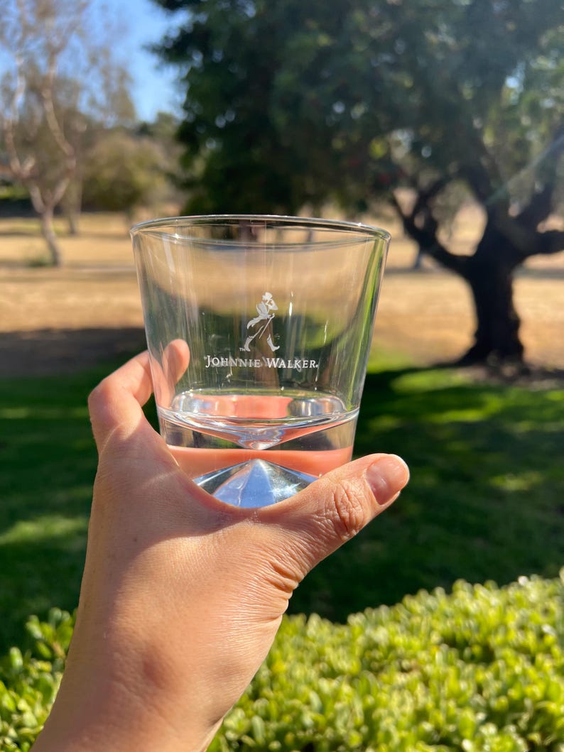 Pu&ograve; includere: Un bicchiere di vetro trasparente con una base a forma di diamante. Il bicchiere ha il logo Johnnie Walker inciso sul lato.
