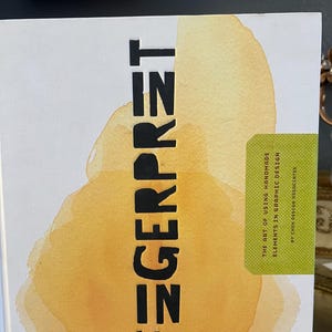 May include: A book titled "FEGERPRET" with large black letters on a white background. The cover features a watercolor design in shades of yellow and orange. The book's subtitle reads "THE ART OF USING HANDMADE ELEMENTS IN GRAPHIC DESIGN."