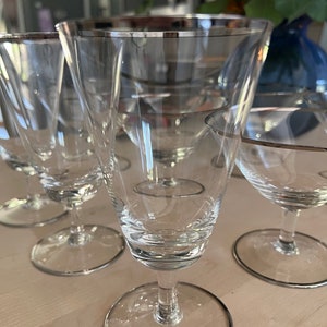 Peut inclure: Ensemble de six verres à boire en verre transparent avec un bord argenté. Les verres sont disposés sur une surface en bois.