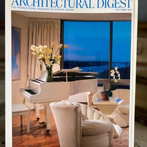 May include: The cover of Architectural Digest magazine, October 2001, features an interior design scene. A white grand piano sits near a window with a view of a bridge. A cream-colored armchair and side table are in the foreground.