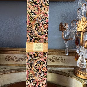 May include: A tall, rectangular box of Mille Fleur drawer liners. The box features a black background with a colorful floral pattern in shades of pink, orange, yellow, and green. The text "Mille Fleur Drawer Liners" is printed on a gold label.