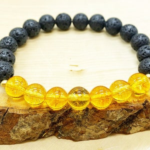 Könnte beinhalten: Armband mit schwarzen Lavasteinperlen und goldgelben Citrinperlen. Das Armband ist auf einem elastischen Band aufgezogen und enthält kleine goldfarbene Akzentperlen. Die Perlen sind rund und haben eine polierte Oberfläche.