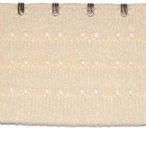 May include: A white bra extender with four metal hooks and eyes. The extender has a textured surface and is designed to adjust the length of a bra strap.