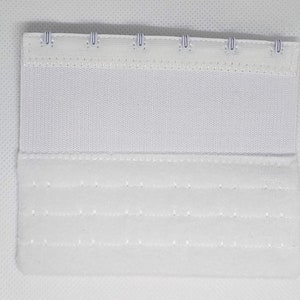 Peut inclure: Une extension de soutien-gorge blanche avec trois rang&eacute;es de fermetures &agrave; crochet et &oelig;illet. L'extension est faite d'un tissu doux et textur&eacute; et pr&eacute;sente une construction robuste. Les crochets sont de couleur argent&eacute;e.