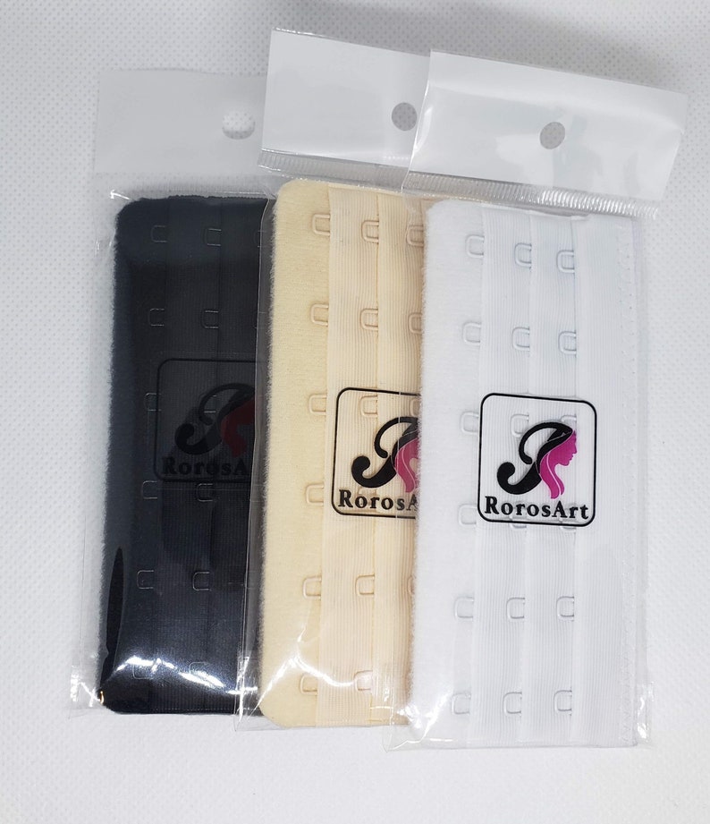 Peut inclure: Trois extensions de soutien-gorge noires, beiges et blanches, chacune emball&eacute;e dans un sac en plastique transparent. Chaque extension comporte trois rang&eacute;es de crochets et d'agrafes. Le logo RorosArt est visible.
