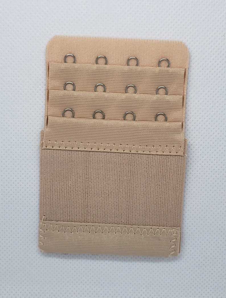 May include: A beige bra extender with three rows of hooks and eyes. Each row has three hooks and eyes.