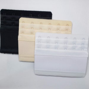 May include: Three bra extenders in black, beige, and white. Each extender has three rows of hook-and-eye closures for adjustable sizing. The extenders are made of a soft, fabric material.