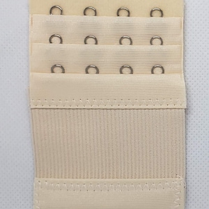 May include: A beige bra extender with three rows of hooks and eyes. Each row has four hooks and eyes.