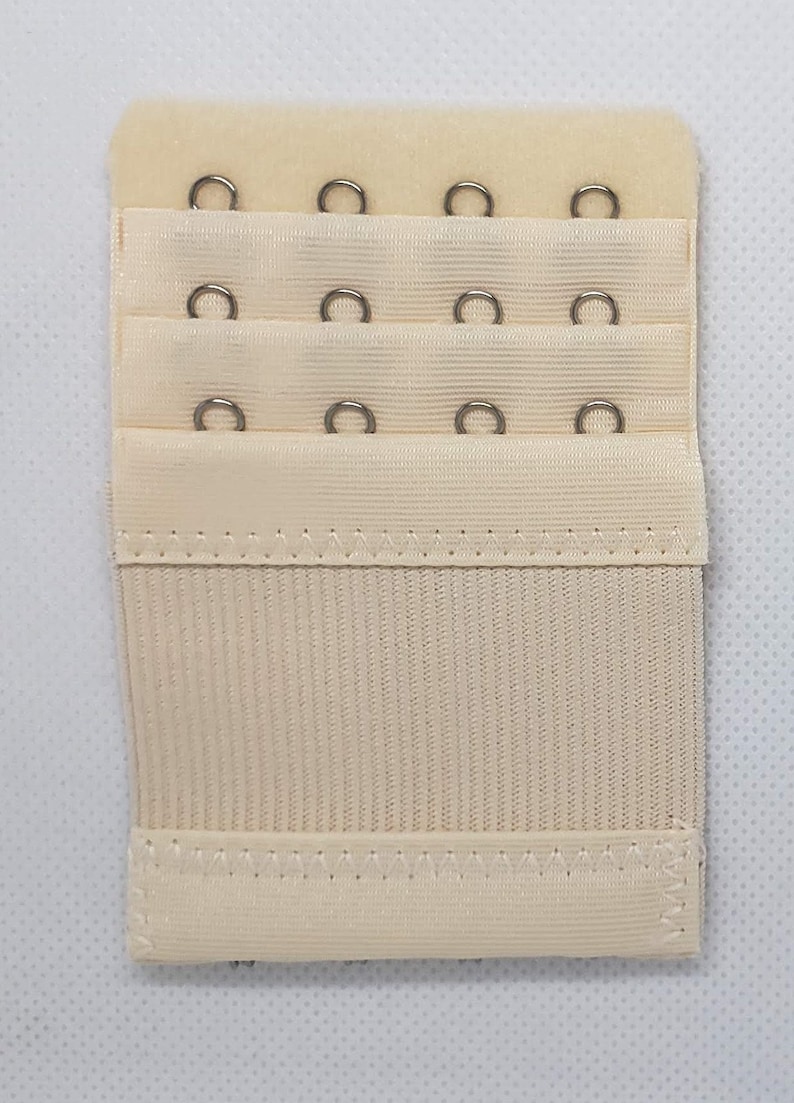 May include: A beige bra extender with three rows of hooks and eyes. Each row has four hooks and eyes.