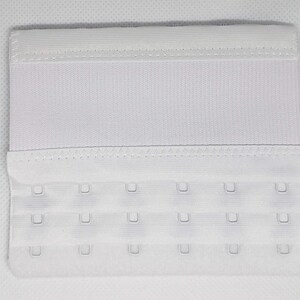 Peut inclure: Une extension de soutien-gorge blanche avec trois rang&eacute;es de fermetures &agrave; crochet et &oelig;illet. L'extension est faite d'un tissu doux et textur&eacute; et comporte une bande &eacute;lastique en haut. Cet accessoire de lingerie ajoute de la longueur &agrave; un soutien-gorge.