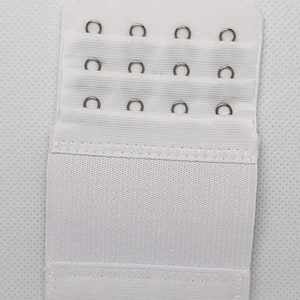 May include: White bra extender with three rows of metal hooks and eyes. The extender is made of a soft, stretchy fabric.