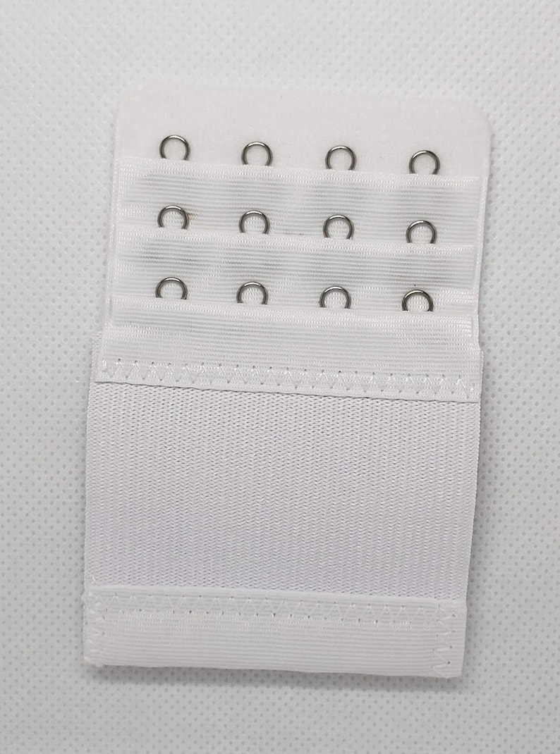 May include: White bra extender with three rows of metal hooks and eyes. The extender is made of a soft, stretchy fabric.