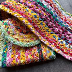 Könnte beinhalten: Ein mehrfarbiger geflochtener Teppich aus verschiedenen Stoffstreifen in Gelb-, Rosa-, Grün-, Blau- und Rottönen. Der Teppich weist eine dichte, gewebte Textur mit einem sich wiederholenden Muster aus geflochtenen Segmenten auf, die in Lagen liegen.