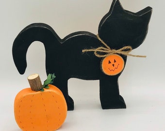 May include: Black wooden cat figurine with a small orange pumpkin with a jack-o'-lantern face. The cat is holding a small orange pumpkin with a jack-o'-lantern face.