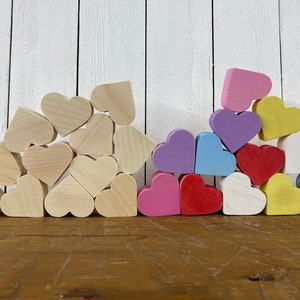 May include: A pile of wooden hearts in various colors, including pink, purple, blue, yellow, and red. The hearts are arranged in a pyramid shape, with the largest heart at the bottom and the smallest heart at the top.