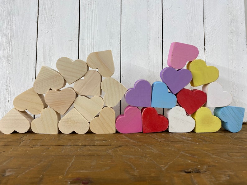 May include: A pile of wooden hearts in various colors, including pink, purple, blue, yellow, and red. The hearts are arranged in a pyramid shape, with the largest heart at the bottom and the smallest heart at the top.
