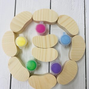 May include: A set of ten wooden bean-shaped ornaments with six small containers of paint in various colors, including pink, yellow, green, blue, and purple.