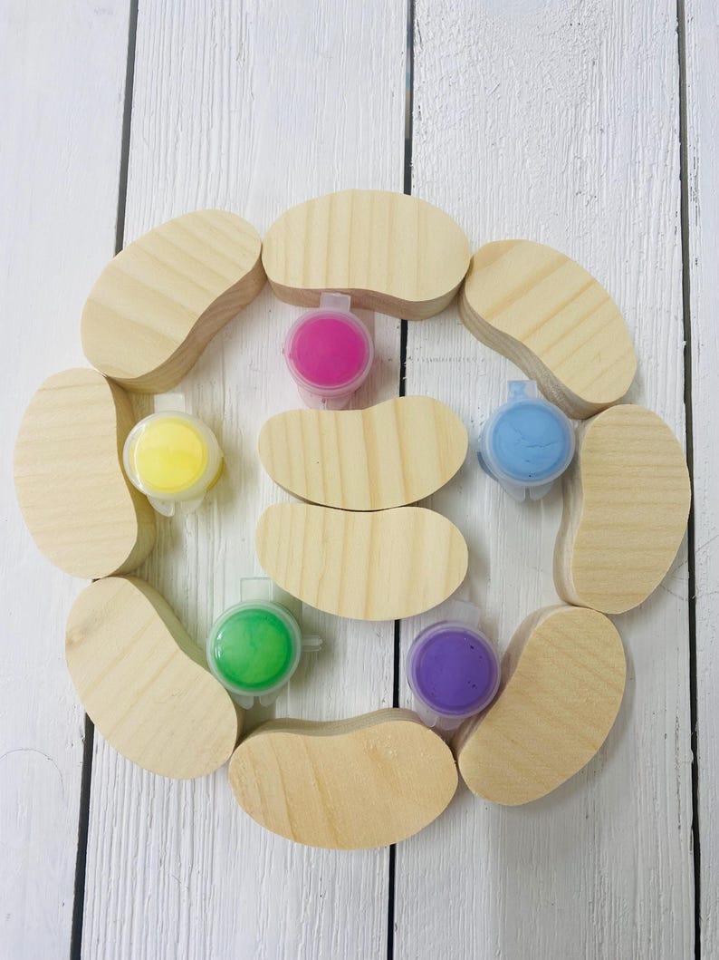 May include: A set of ten wooden bean-shaped ornaments with six small containers of paint in various colors, including pink, yellow, green, blue, and purple.