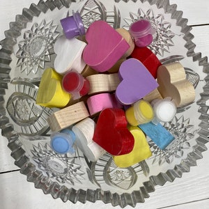 May include: A glass bowl filled with wooden heart shapes in various colors, including pink, purple, yellow, red, and white. Small paint pots in different colors are also included.