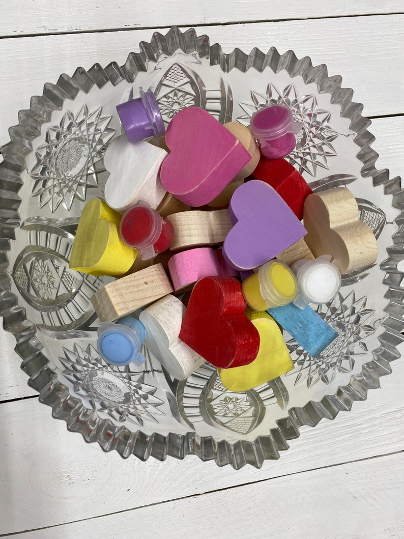 May include: A glass bowl filled with wooden heart shapes in various colors, including pink, purple, yellow, red, and white. Small paint pots in different colors are also included.