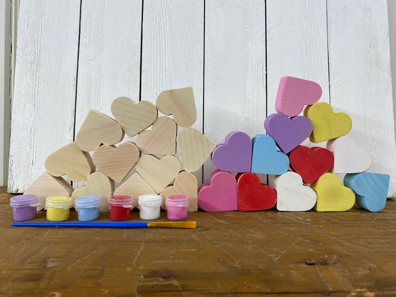 May include: A set of wooden heart-shaped craft blanks with six small paint pots and a paintbrush. The hearts are arranged in a pyramid shape and are ready to be painted.