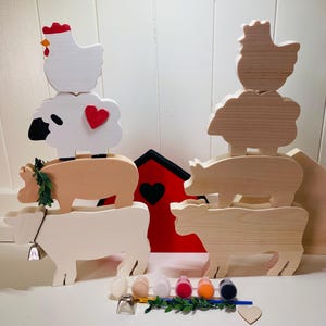 May include: A wooden farm animal stacking toy set with a red barn, a cow, a pig, a sheep, and a chicken. The set includes paint and a paintbrush for painting the animals.