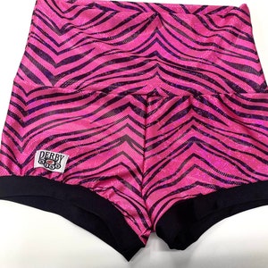 May include: Pink and black zebra print shorts with a black waistband and a black trim around the leg openings. The shorts have a small white patch with the text "Derby Kiss" in black.
