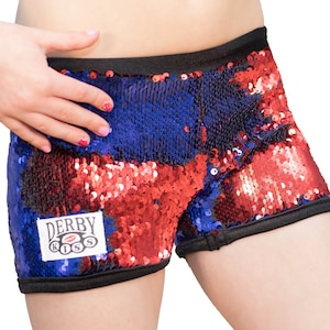 May include: Red, blue, and black sequined shorts with a black waistband and a black trim. The shorts have a logo patch that says "Derby Kiss" with a red lip print.