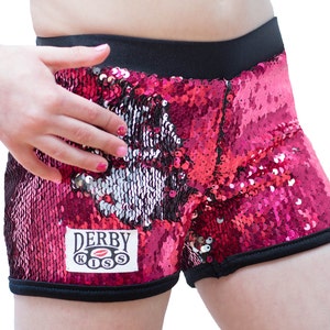 May include: Pink and silver sequined shorts with a black waistband and black trim. The shorts have a patch on the front that says "Derby Kiss" with a red lip logo.
