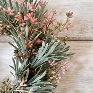 May include: A green and pink artificial floral wreath with small pink flowers and green leaves.