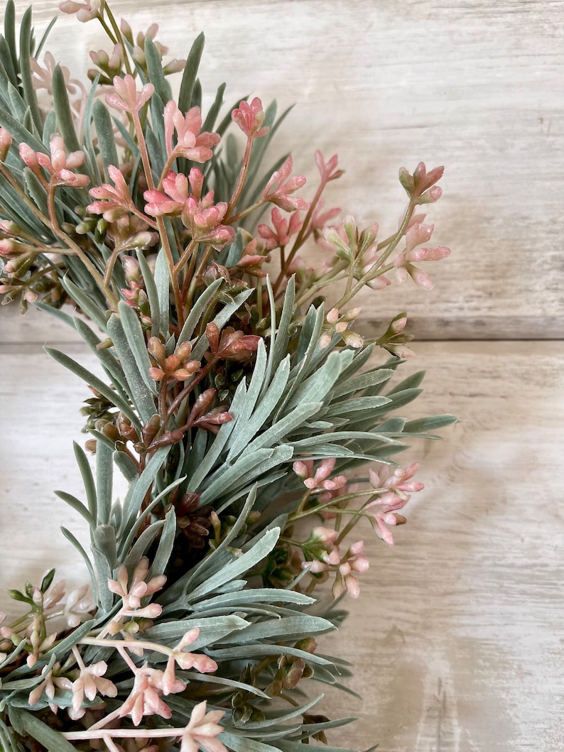 May include: A green and pink artificial floral wreath with small pink flowers and green leaves.