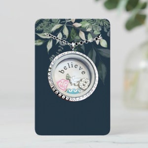 May include: Silver locket necklace with a clear glass insert. The locket has a silver chain and is decorated with rhinestones. The glass insert has the word "believe" written on it and contains several small charms, including a dove, a wave, and a heart with the letters "CTR" on it.